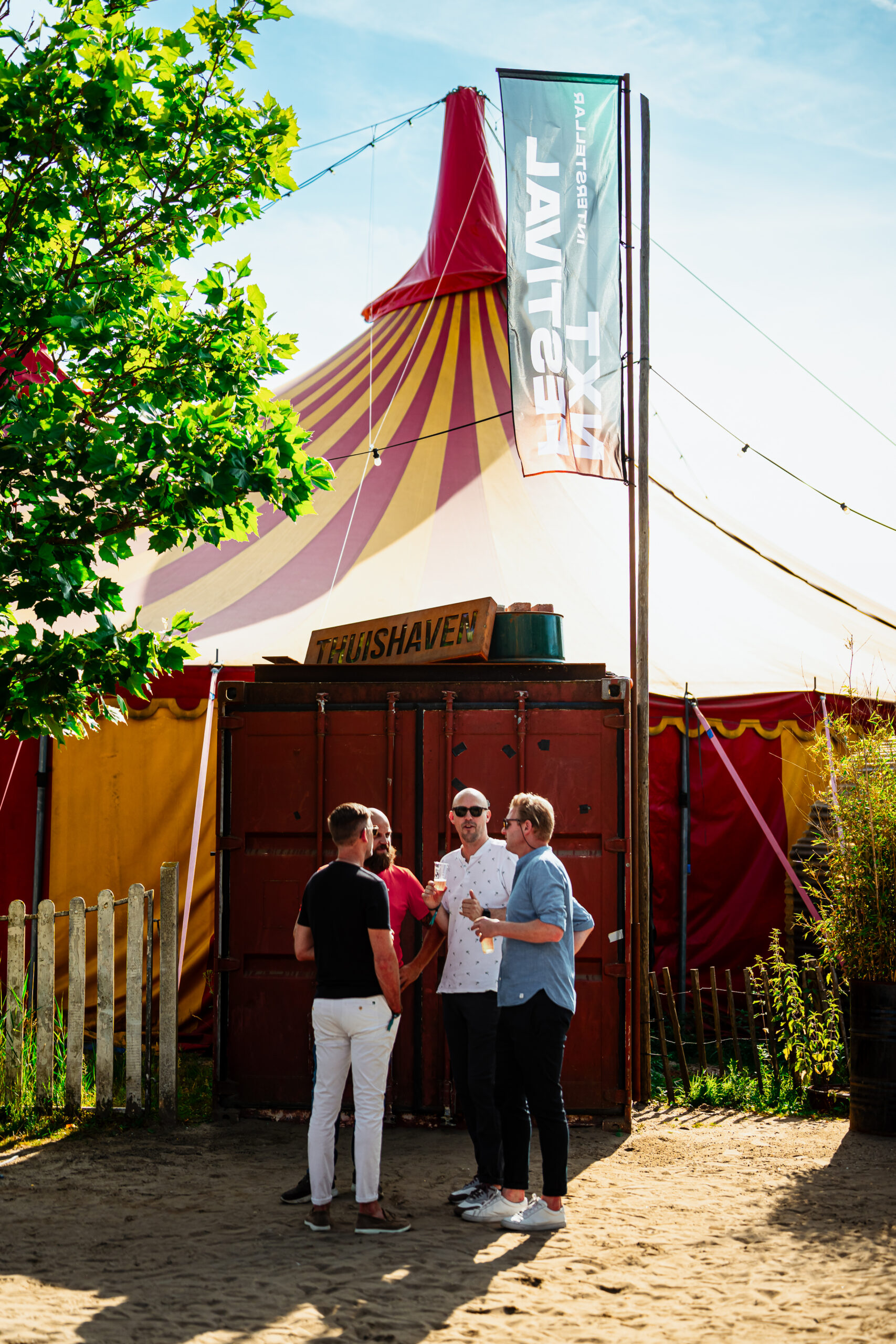 Gezellig festivalgesprek bij de ingang van een grote rood-gele circustent.