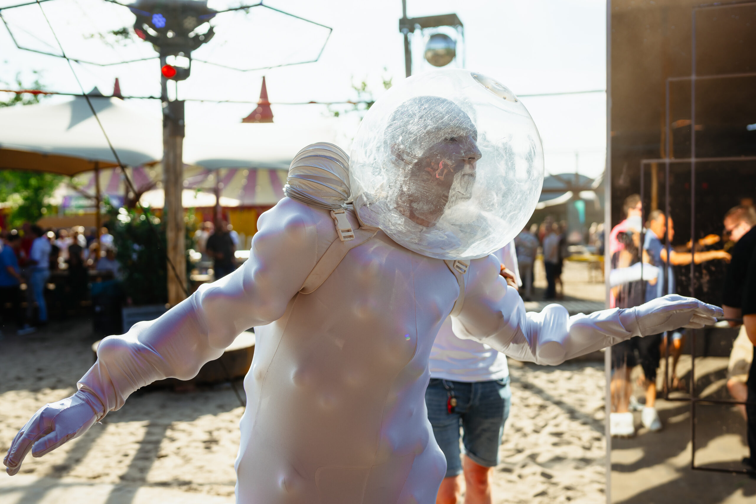 Een performer in een futuristisch astronautenkostuum entertaint festivalgangers.