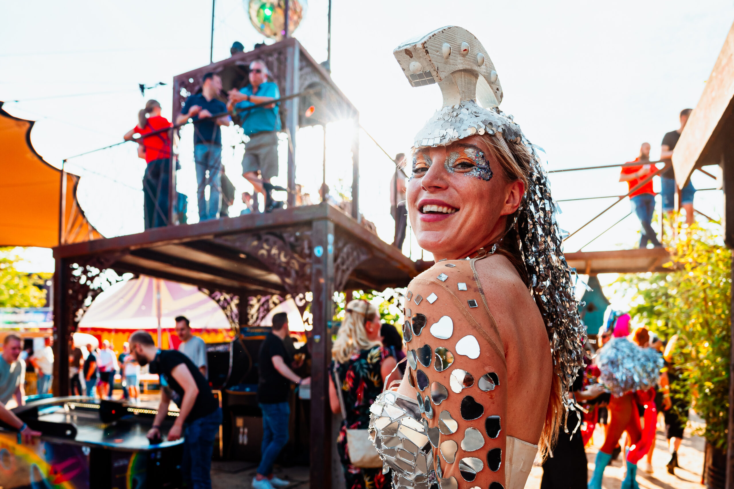 Een performer in een zilveren outfit straalt op een kleurrijk festival.