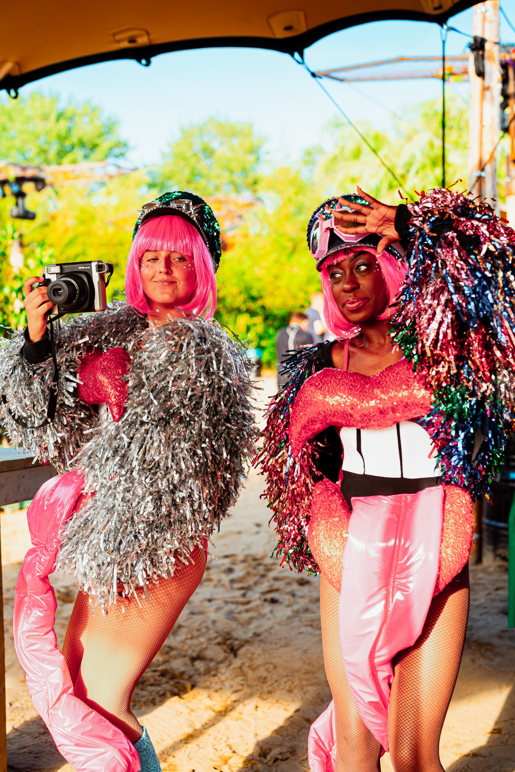 Twee vrouwen in opvallende roze en zilveren outfits met camera.