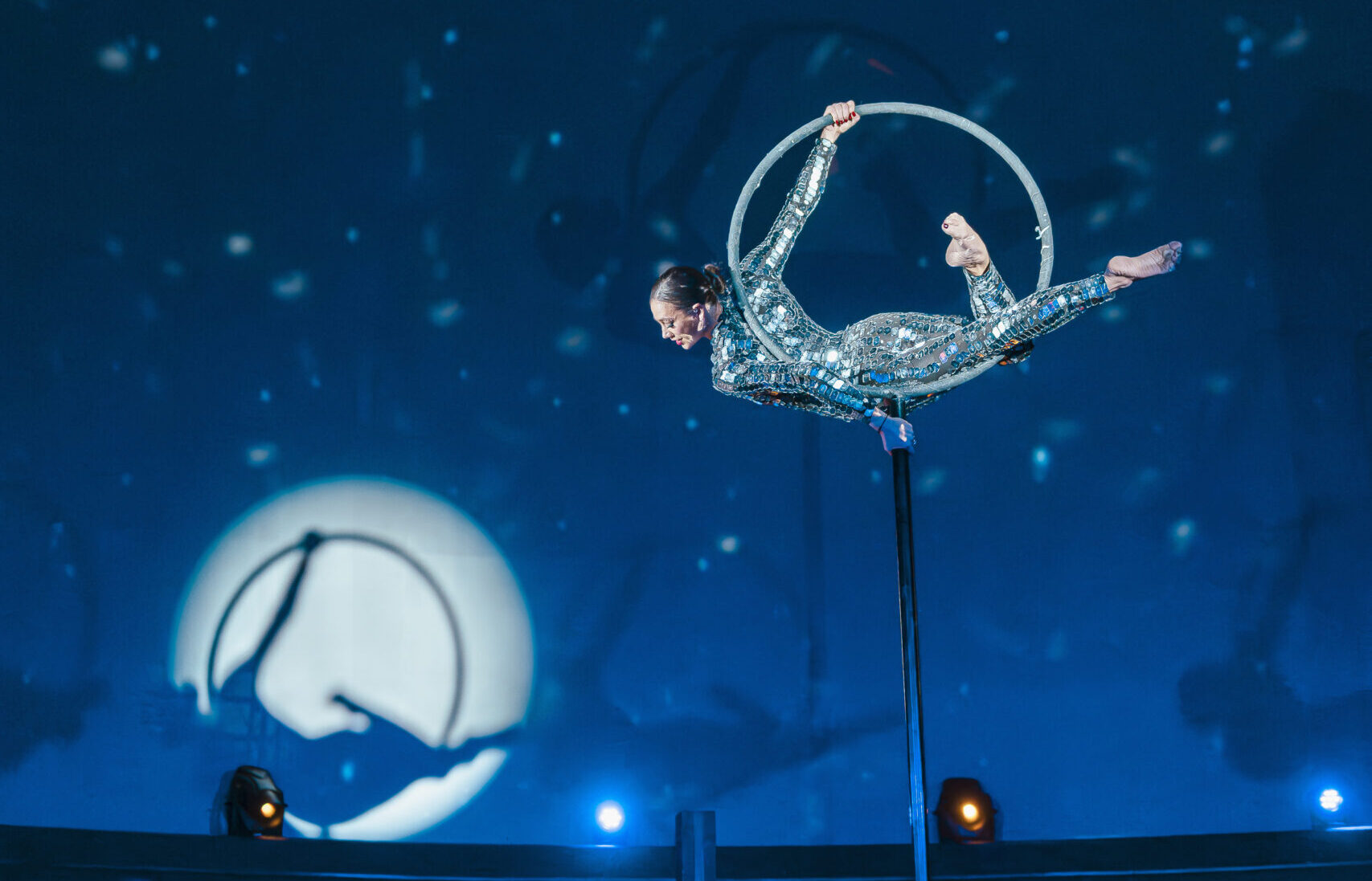 Acrobate in een sprankelend kostuum voert een act uit in een hoepel tegen een blauw verlichte achtergrond.