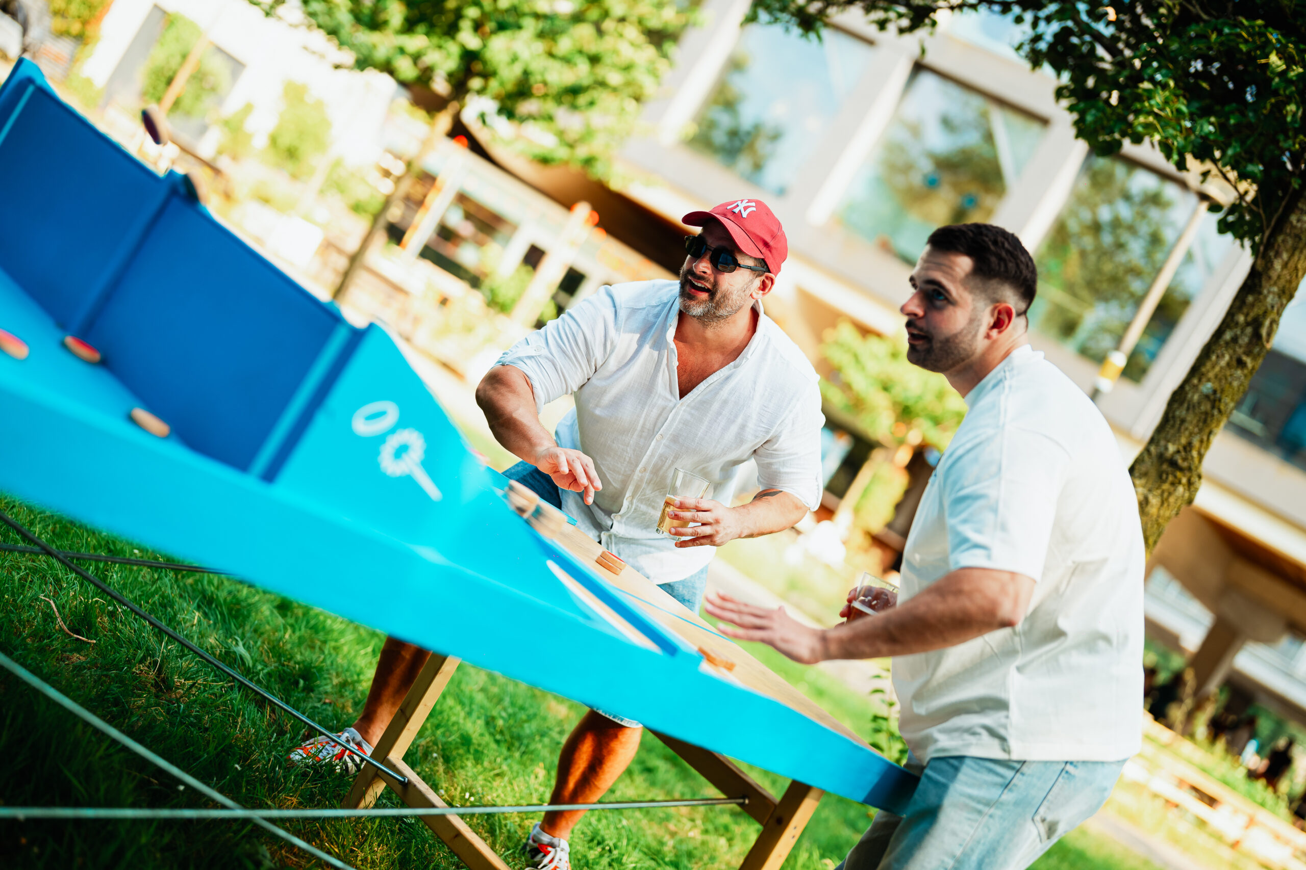 Twee mannen spelen een actief spel aan een blauwe speeltafel tijdens een zomers evenement op het gras.