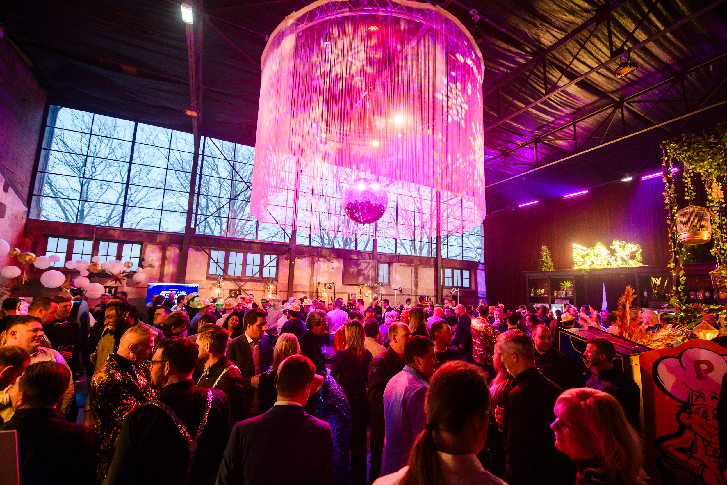 Grote discobal met roze verlichting boven een drukke ruimte.