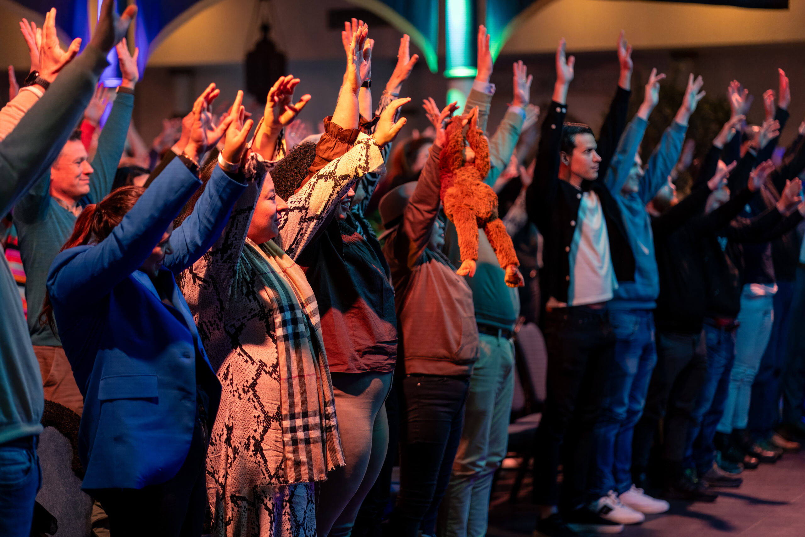 Groep mensen steekt enthousiast hun handen in de lucht tijdens een motiverende sessie.