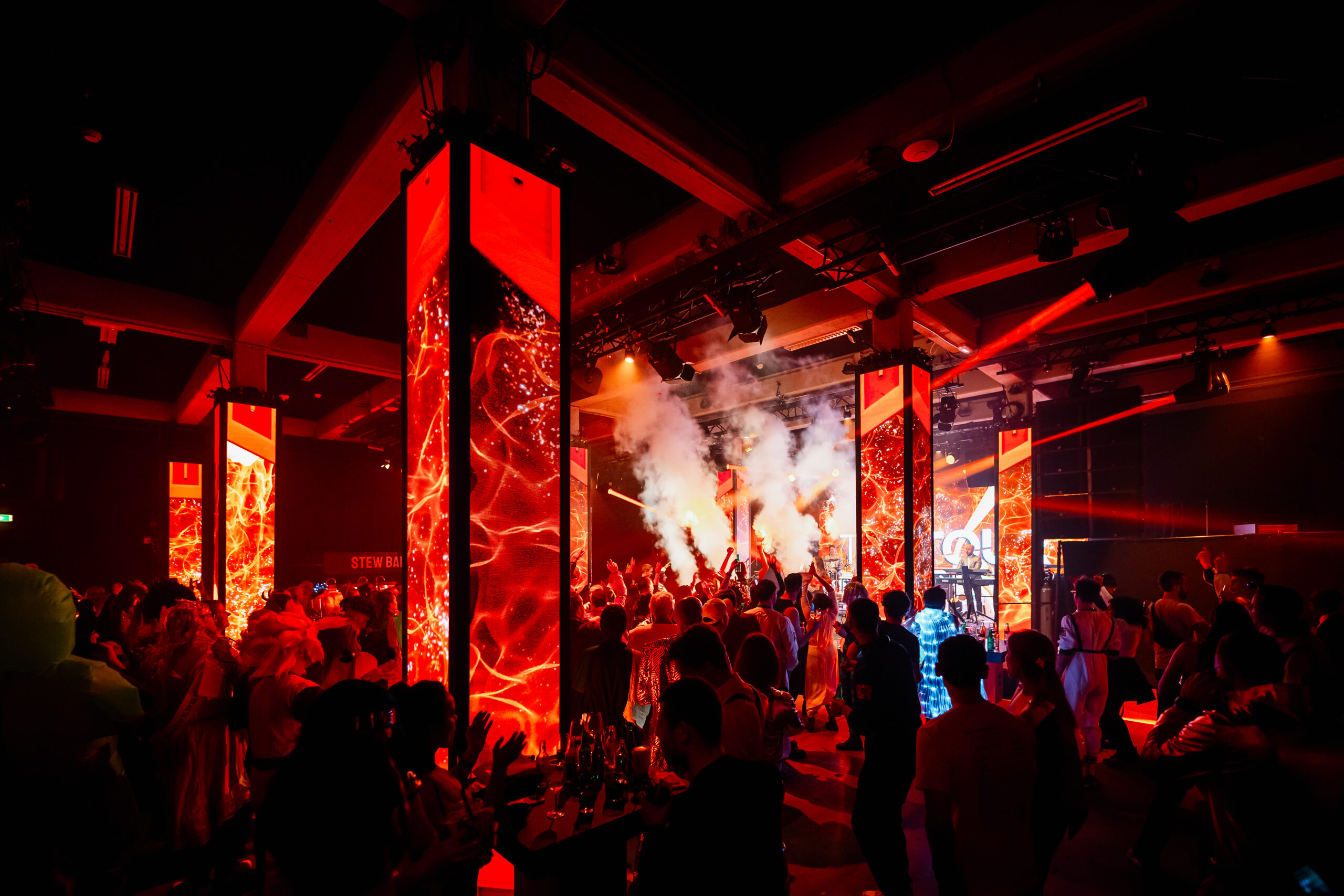 Rood verlichte pilaren en lichteffecten tijdens een groots themafeest.