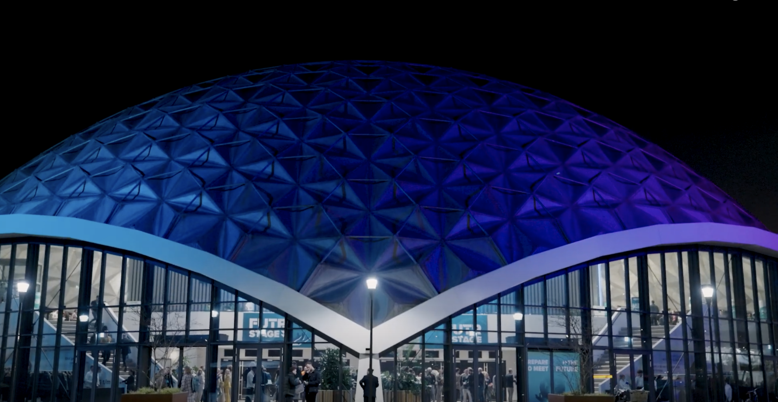 Een futuristische koepelvormige evenementenlocatie, verlicht in blauw en paars.