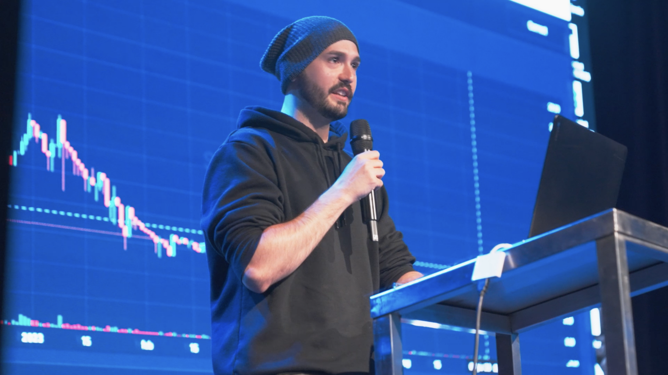 Hackathon Aptos - Een spreker presenteert met een grafiek op de achtergrond tijdens de Aptos hackathon.