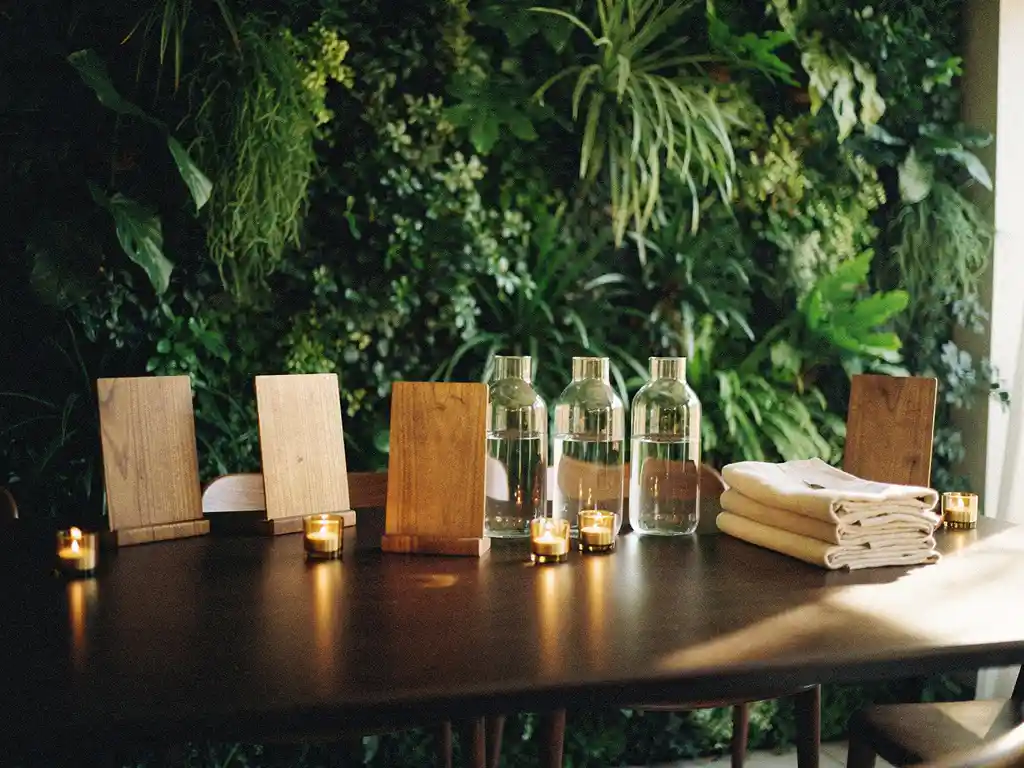 Weelderige plantenwand als achtergrond voor een duurzame brandevenement opstelling met houten displays, glazen waterdispensers en linnen servetten.